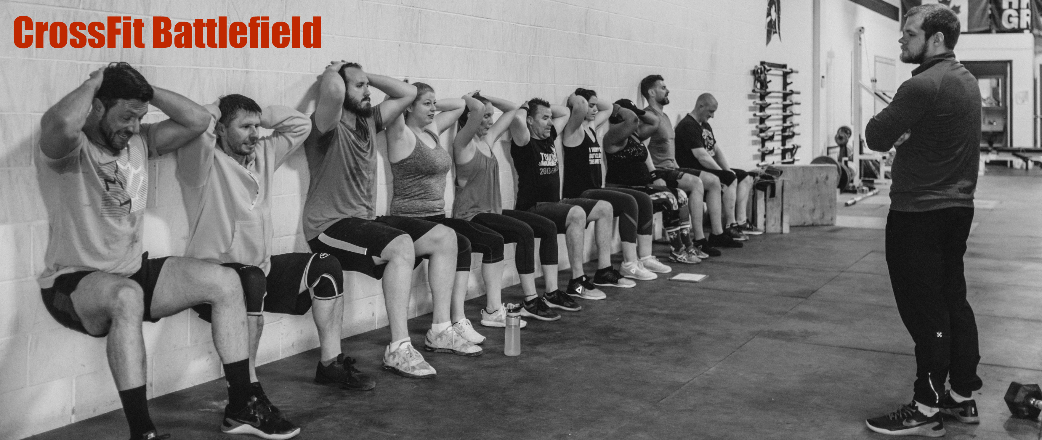 People doing wall squats at the Crossfit Battlefield gym while a coach watches