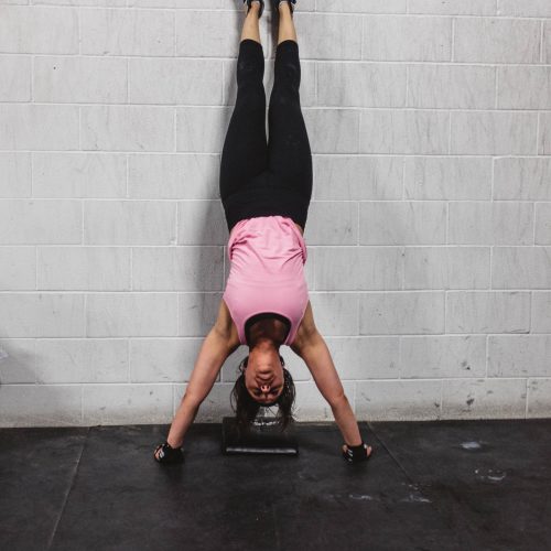 A woman in a pink shirt doing a headstand against a wall