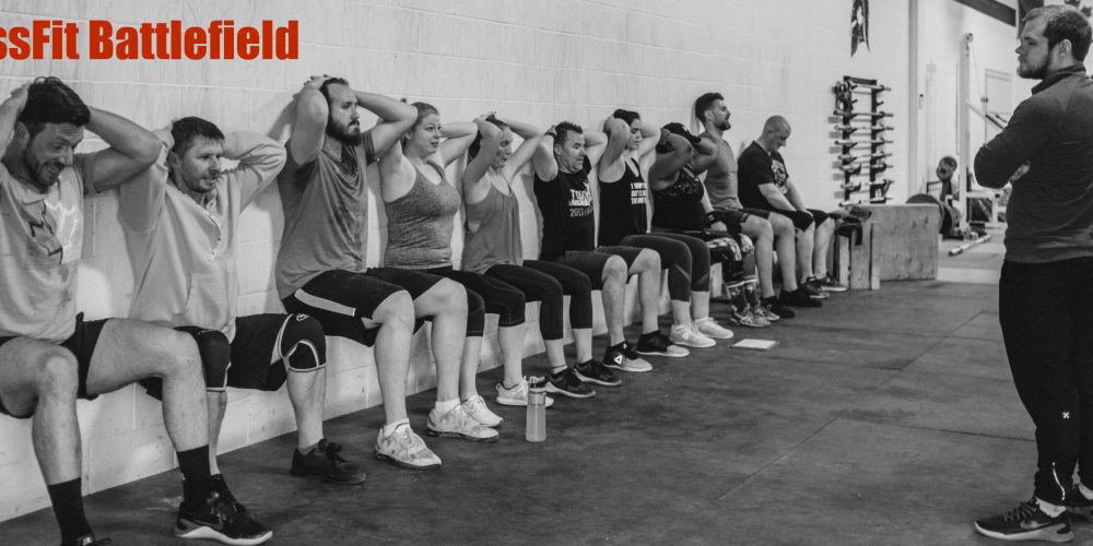 People doing wall squats at the Crossfit Battlefield gym while a coach watches